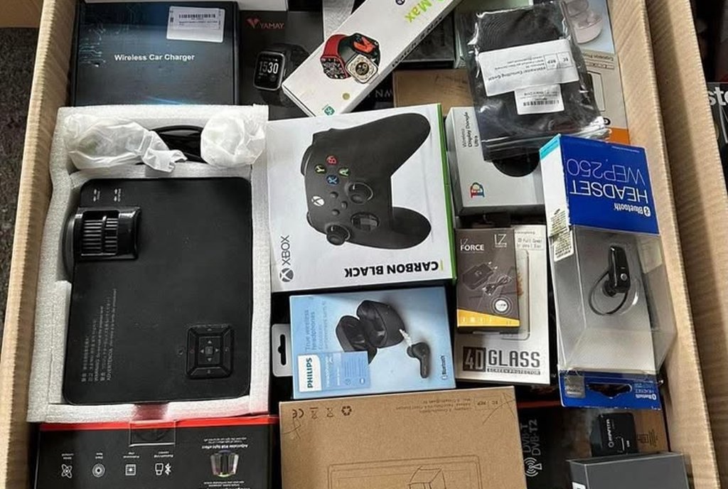 Caixa de papelão cheia de eletrônicos: câmera de ação, controle de videogame, fones e carregadores lacrados